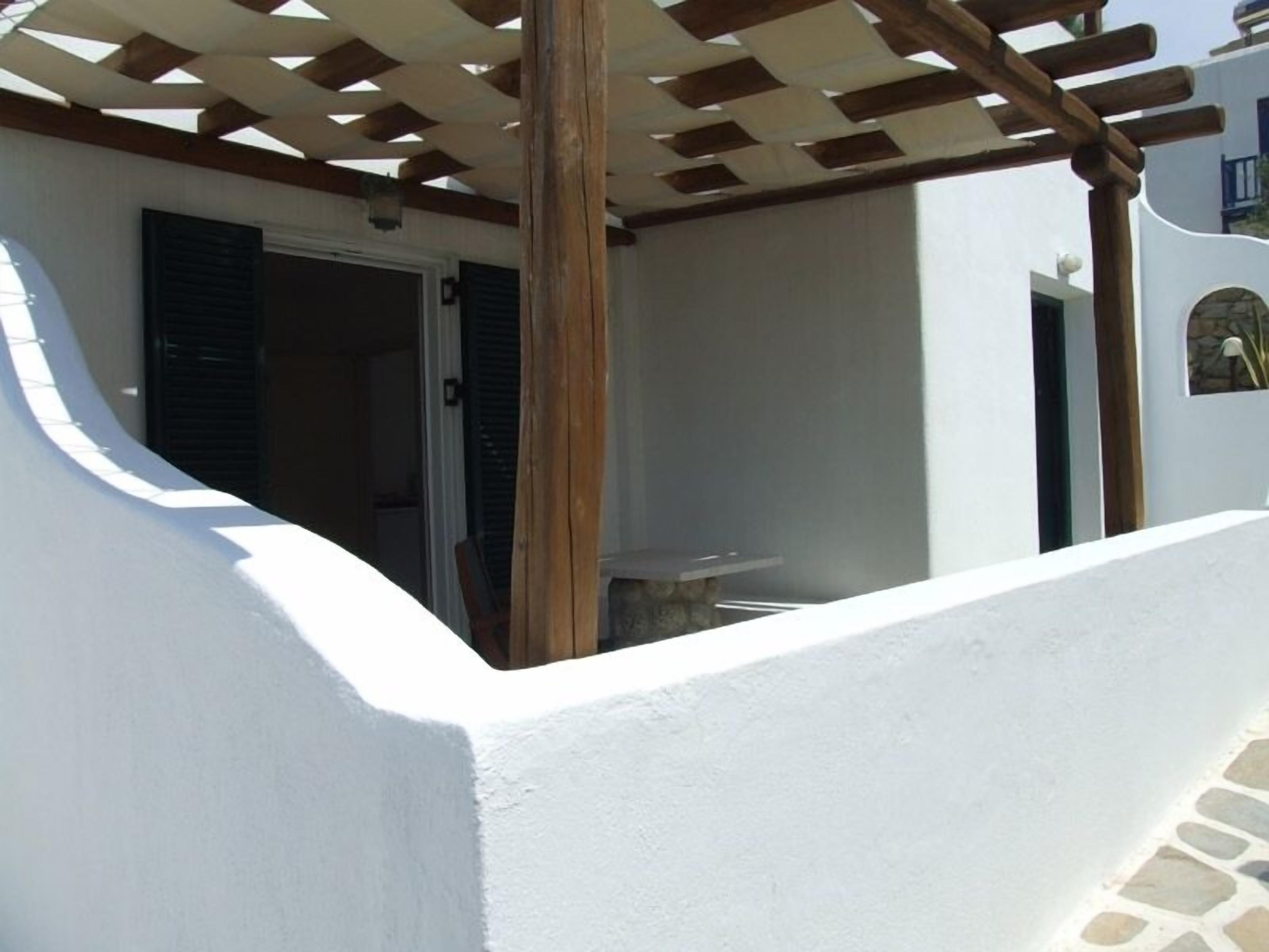 Un espacio exterior techado con una estructura de pérgola, una pared blanca y un suelo de piedra.