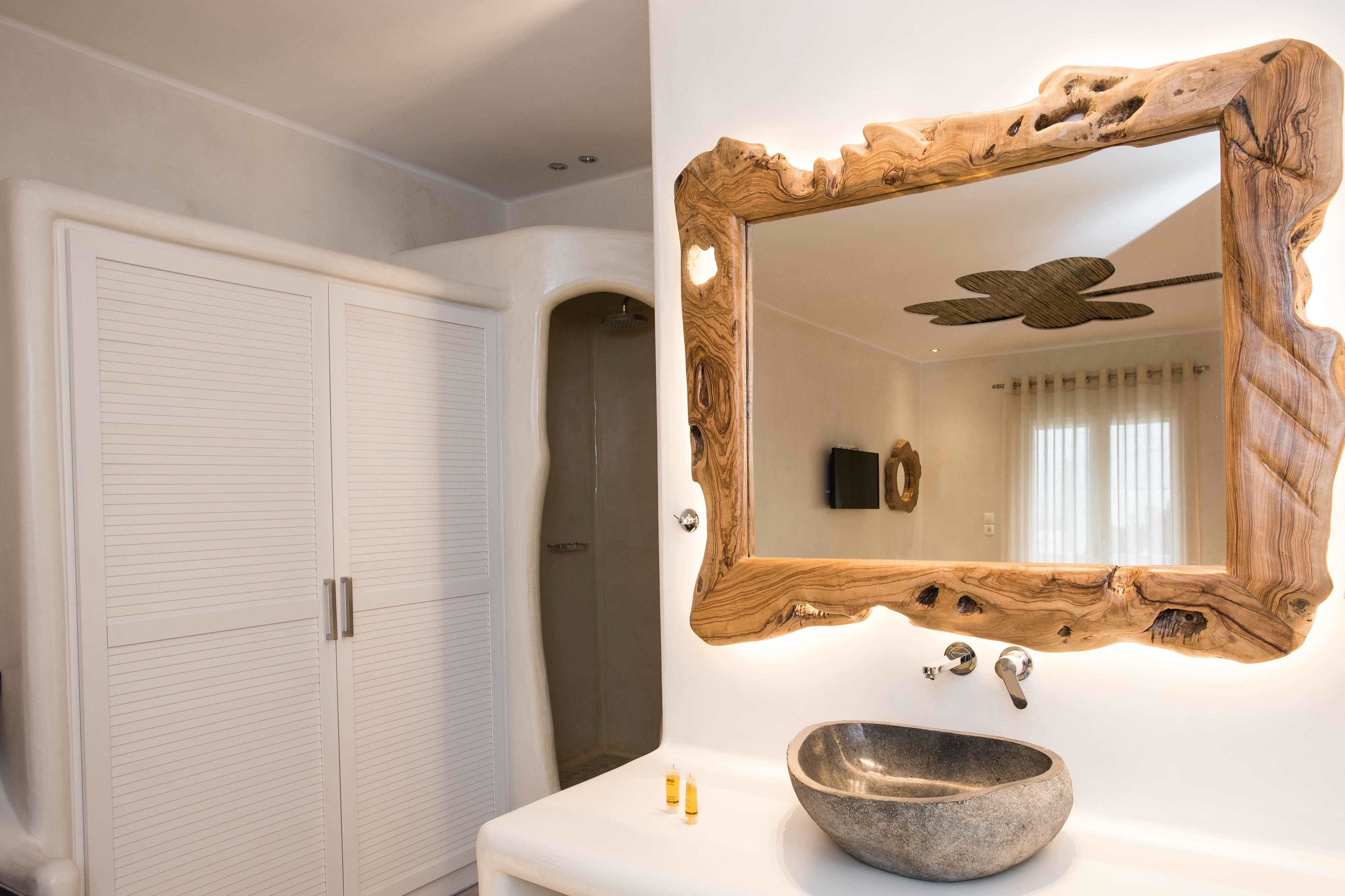 Un baño con espejo de marco de madera, lavabo de piedra y ducha.