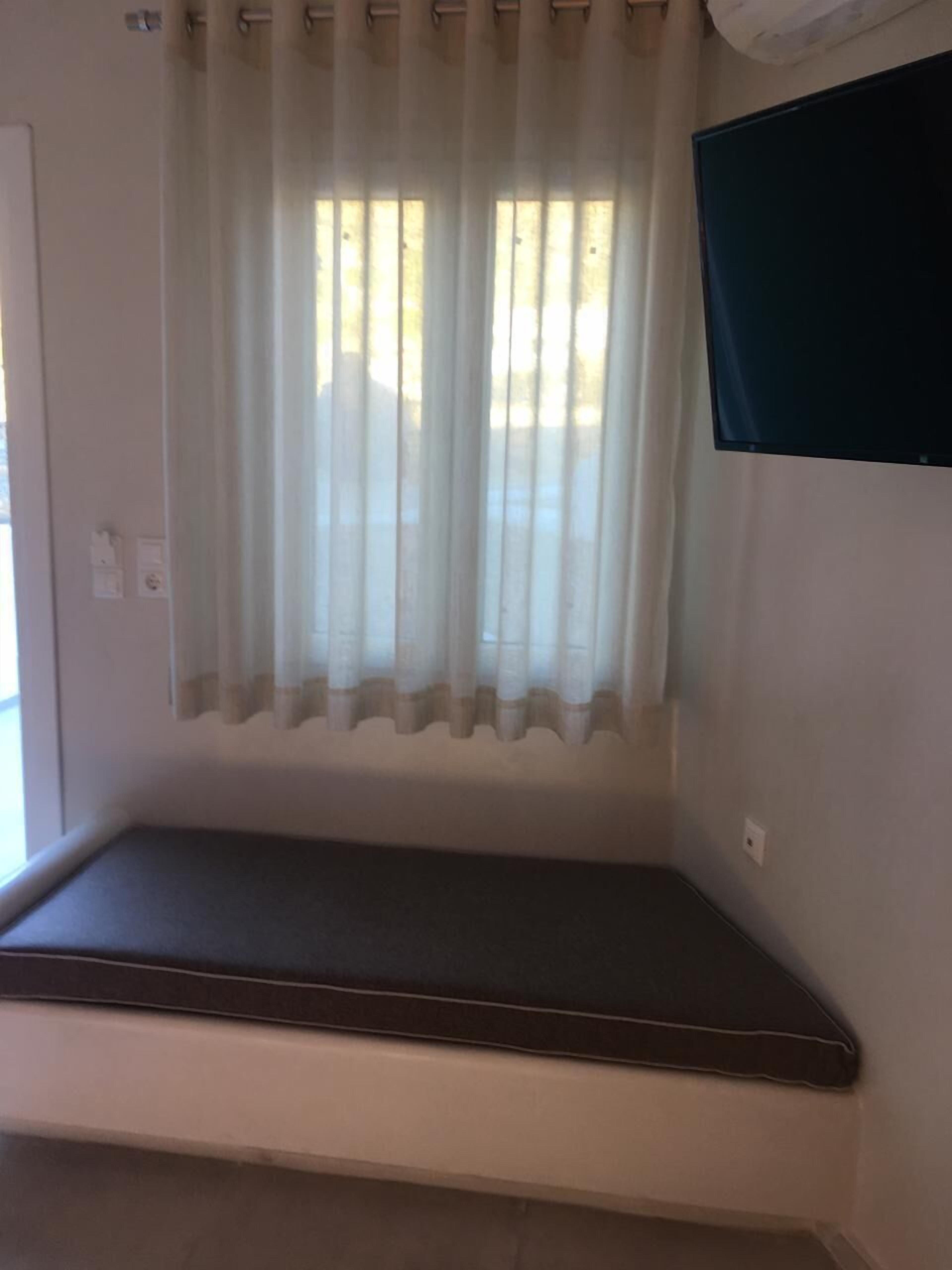 A room with a window, a bench, and a wall-mounted TV.