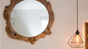 Ein spiegel mit Holzrahmen, ein Holztisch mit rundem Tablett und eine weiße Bank.