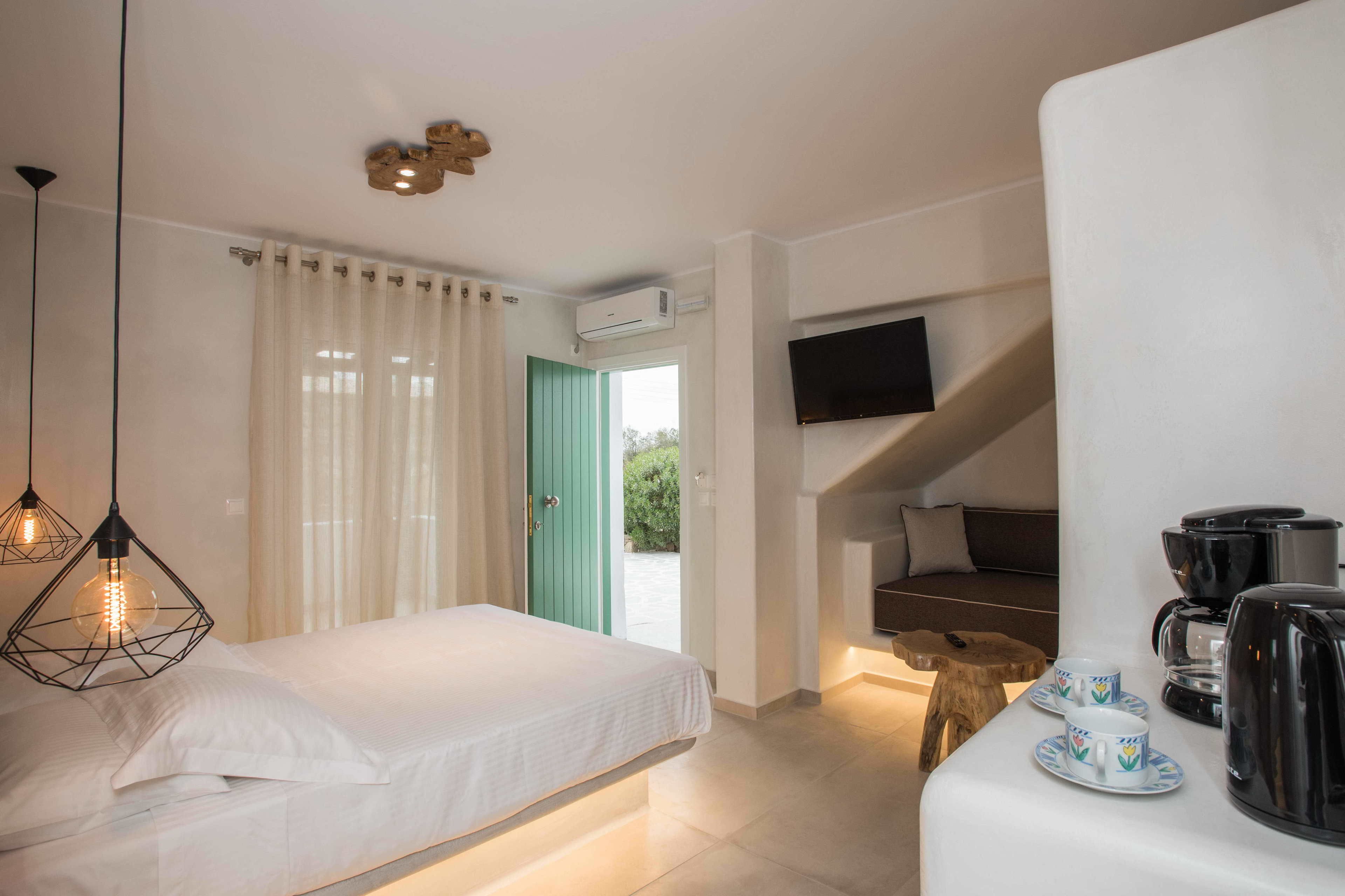 Habitación de hotel moderna con cama, televisor montado en la pared, cafetera y vistas al exterior.