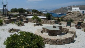 Eine Küstenresortanlage mit Steinsitzgelegenheiten, einem zentralen Steintisch und Blick auf das Meer und Boote.