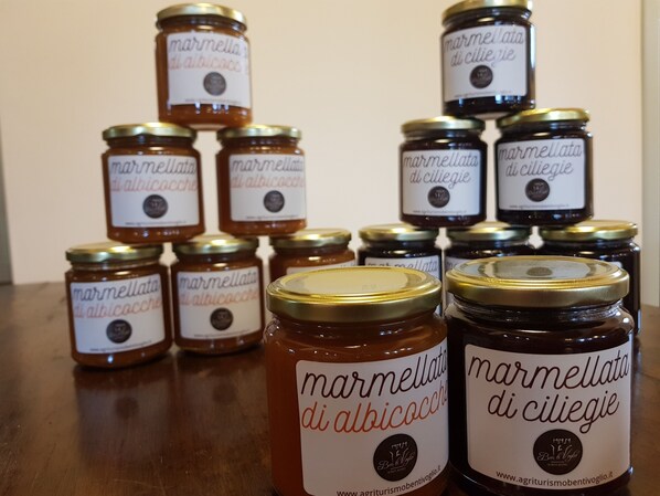 A collection of jars labeled 'marmellata di albacocche' and 'marmellata di ciliegie' arranged on a wooden surface. - Agriturismo Ben Ti Voglio (Bologna)