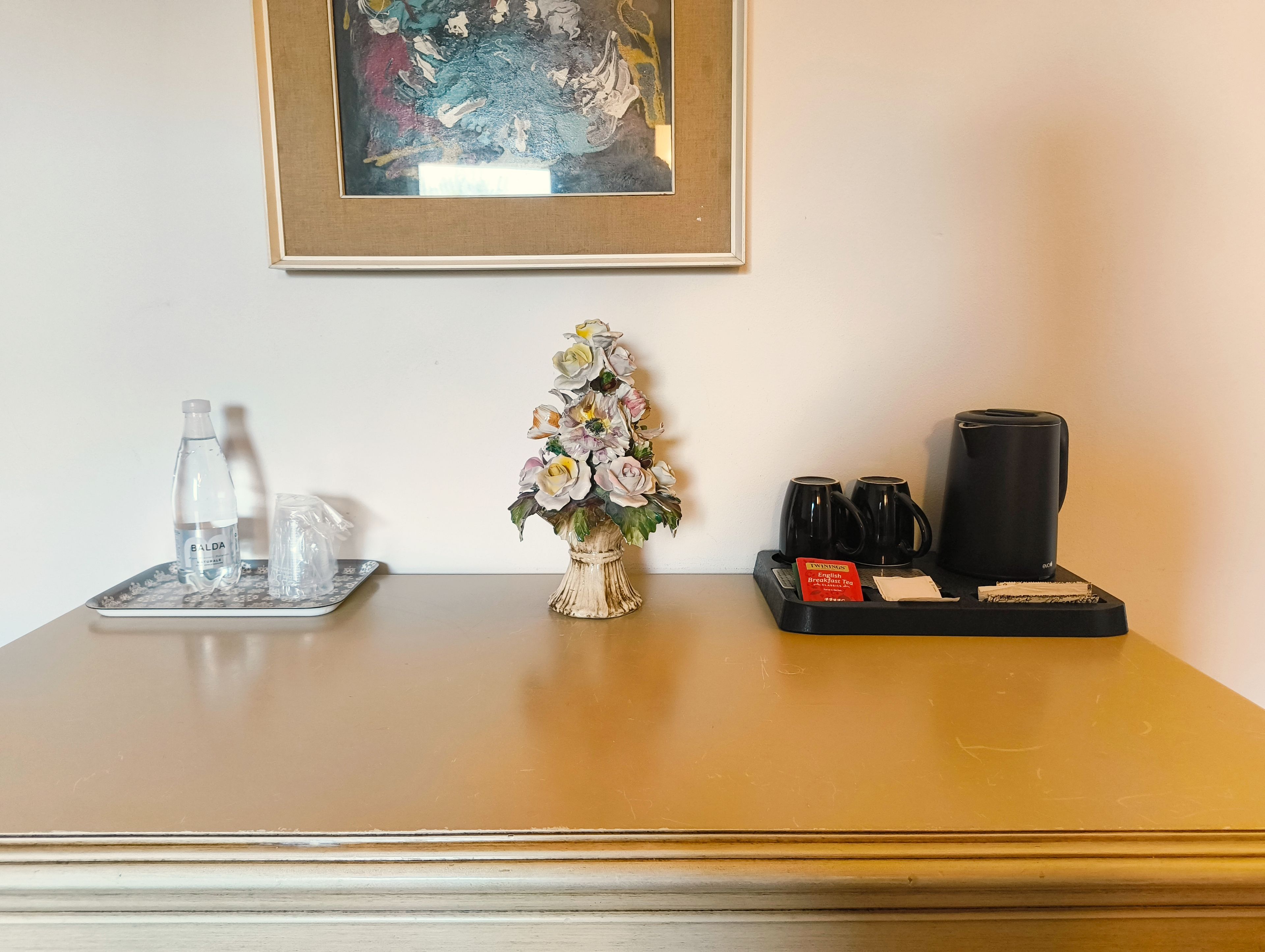 A table with a water bottle, a glass, a tray with a coffee maker, cups, and a tea packet.
