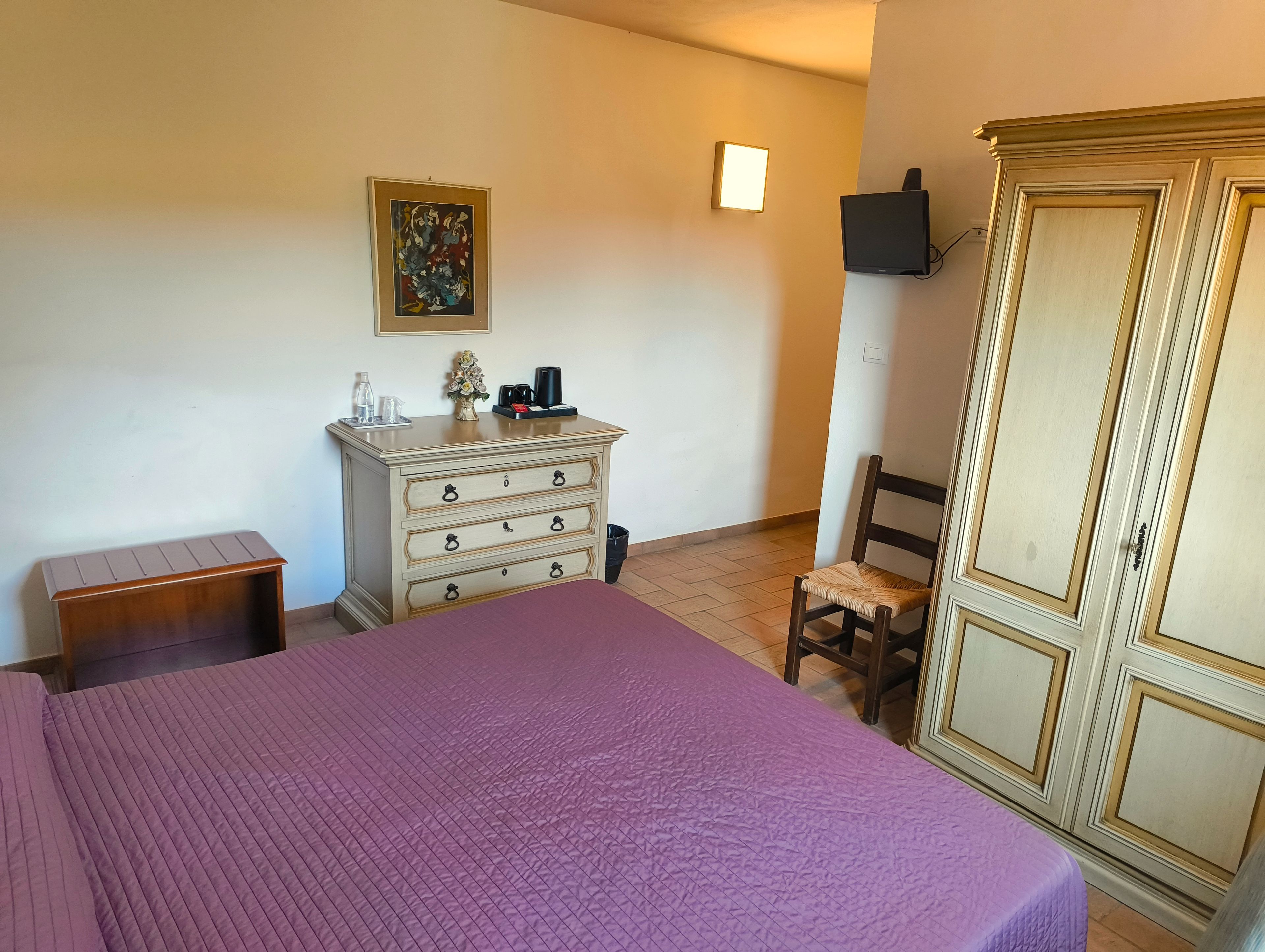 A bedroom with a bed, dresser, chair, wardrobe, and a painting on the wall.