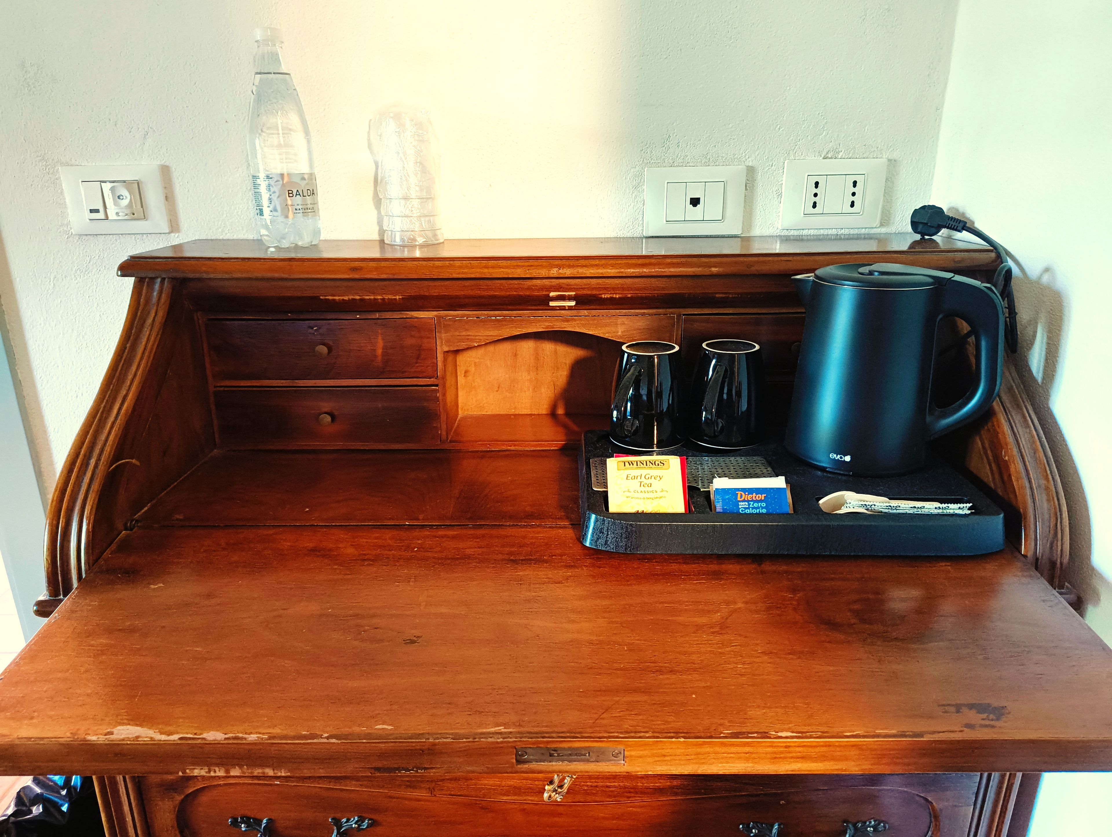 A wooden desk with a coffee maker, tea packets, and a water bottle.