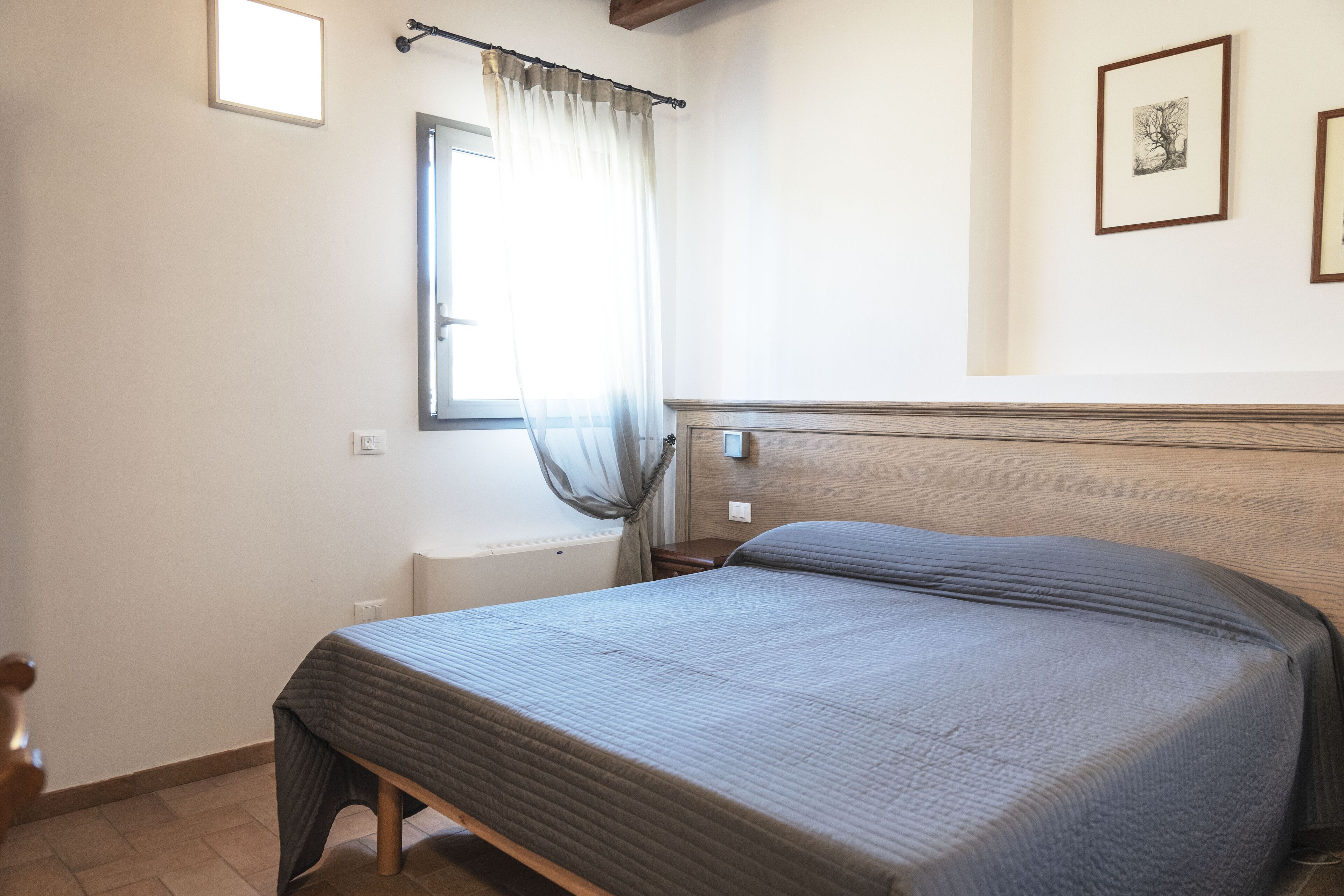 A bedroom with a bed, a window with curtains, a bedside table, and a wall-mounted light fixture.