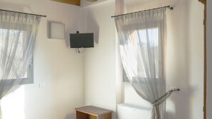 Een kamer met een bed, een houten tafel, een aan de muur bevestigde televisie en een raam met dunne gordijnen.