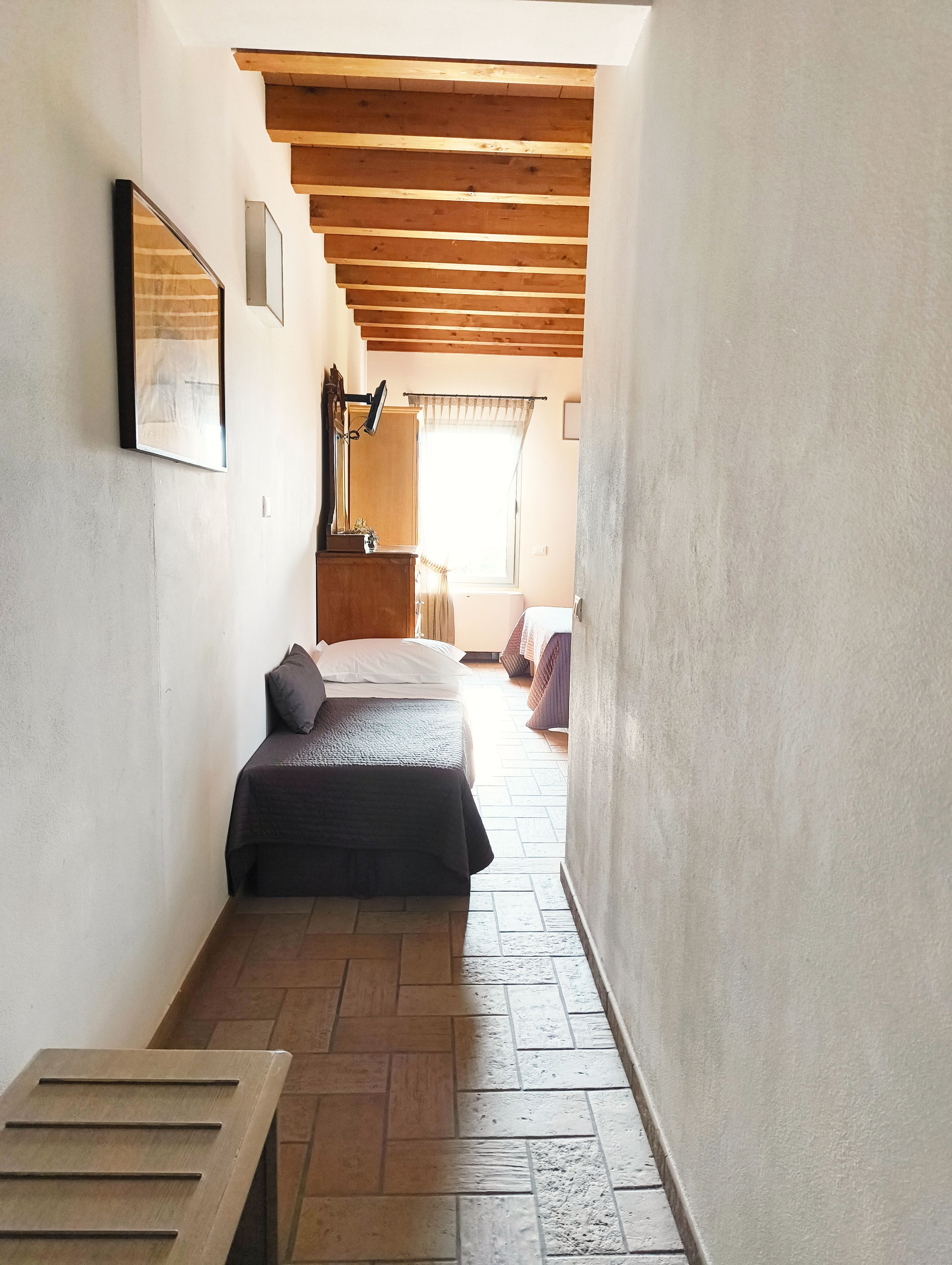 A narrow hallway leading to a bedroom with a bed, a wooden bench, and a radiator.