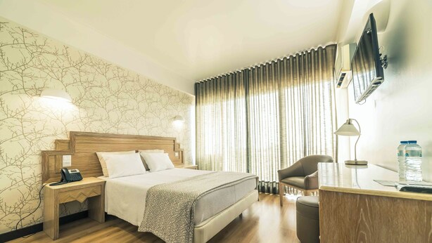 Habitación de hotel con cama, mesita de noche con teléfono, escritorio con lámpara, silla y televisor montado en la pared.