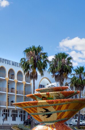 A hotel with a fountain in front, palm trees, and a clear blue sky. - Hotel Melius (Beja)