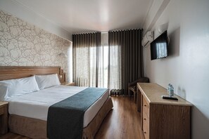 Habitación de hotel con cama, escritorio, silla, televisor y ventana con cortinas.