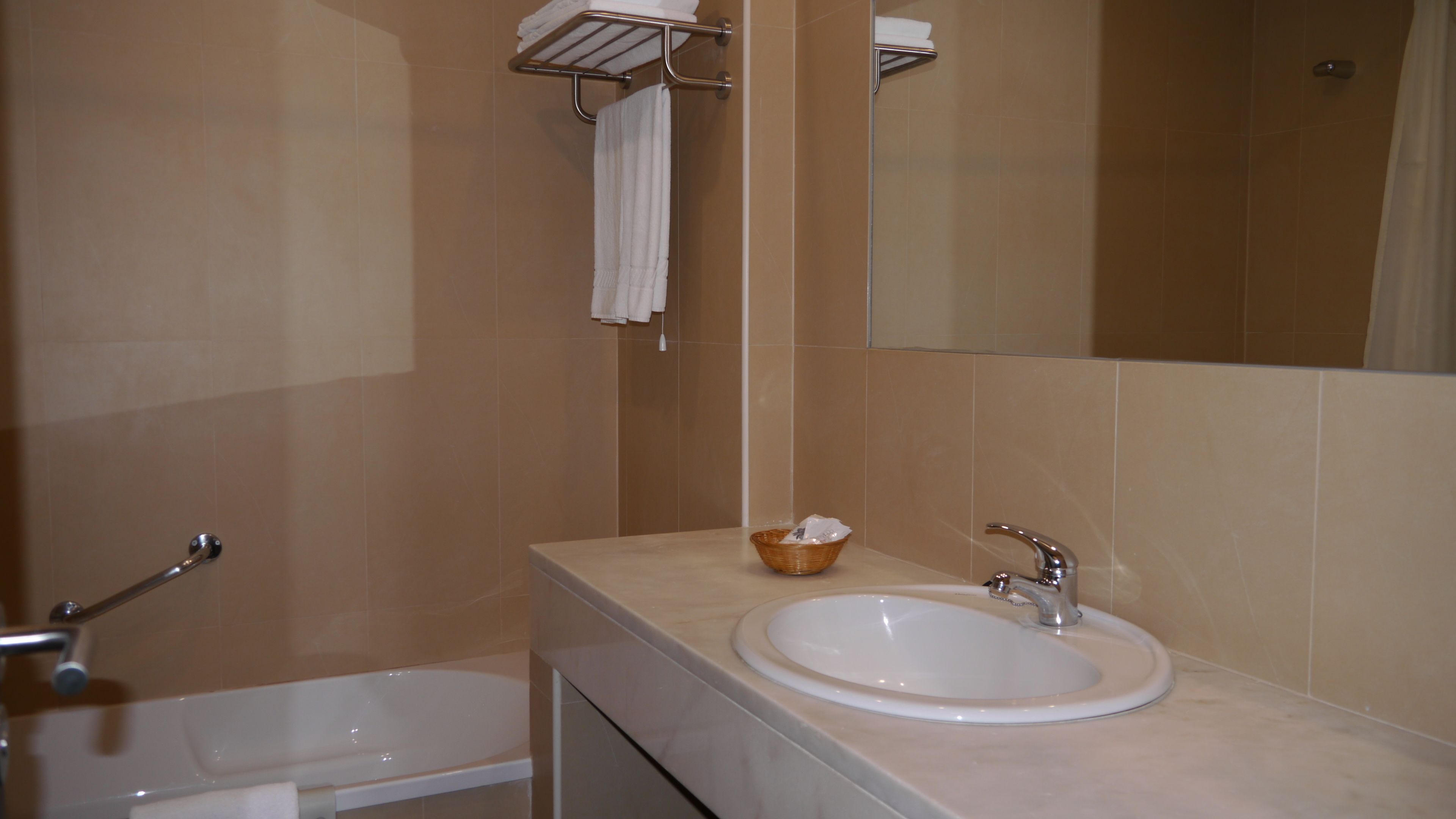 Un baño con un lavamanos blanco, un espejo y un perchero para toallas.