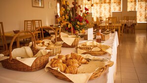 Un comedor con mesas dispuestas para el desayuno, con cestas de pan y pasteles.