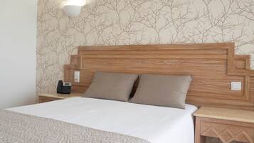 Una cama bien hecha con una colcha estampada, cabecera de madera, dos almohadas, un teléfono en la mesita de noche y una lámpara.
