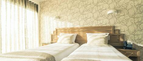 A hotel room with two beds, a wooden headboard, a telephone, and a wall with a tree branch pattern.