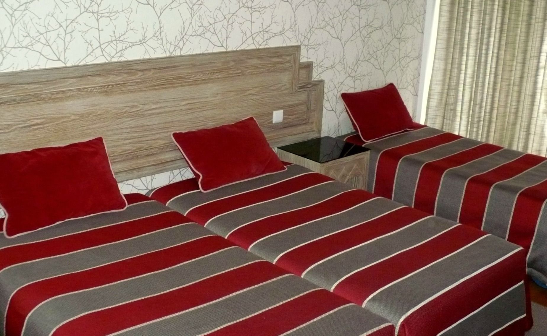 A hotel room with two beds, each with red and grey striped bedding, a wooden headboard, and a nightstand with a lamp.