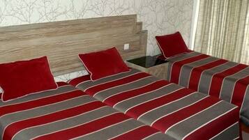 A hotel room with two beds, each with red and grey striped bedding, a wooden headboard, and a nightstand with a lamp.
