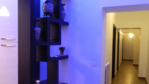 A hallway with a blue-lit shelving unit displaying decorative items. - Romangelo 2 Hostel (Rome)