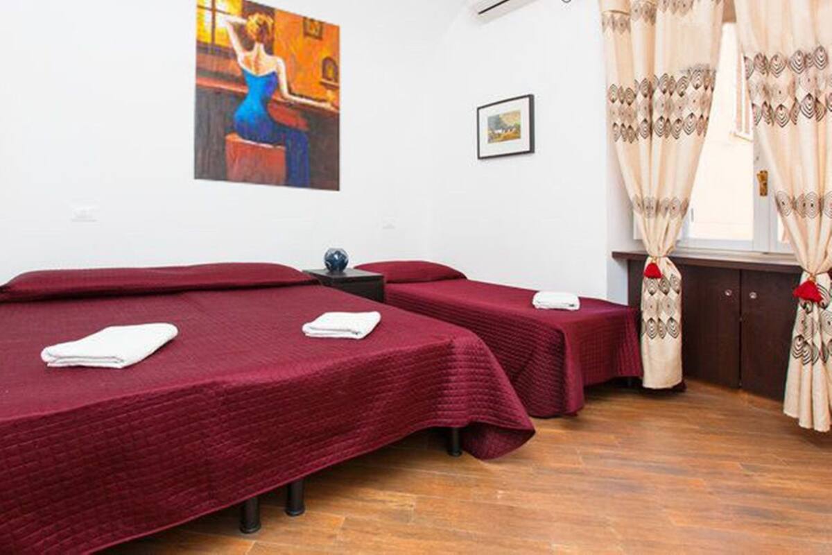 A room with two single beds, a small table, a painting on the wall, and curtains.
