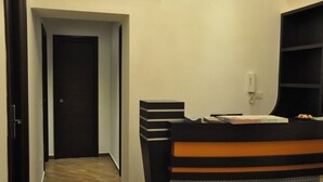 A hotel reception area with a reception desk, a telephone, and a door leading to another room. - Romangelo 2 Hostel (Rome)
