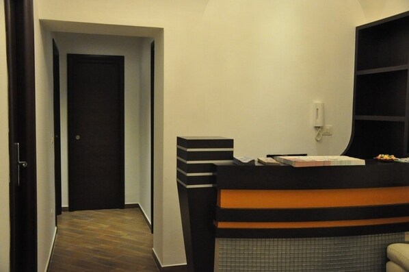 A hotel reception area with a reception desk, a telephone, and a door leading to another room. - Romangelo 2 Hostel (Rome)