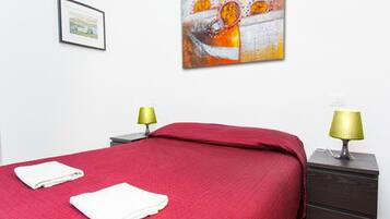 Ein Hotelzimmer mit roter Bettdecke, zwei weißen Handtüchern, einem gerahmten Bild an der Wand und zwei Nachttischlampen.
