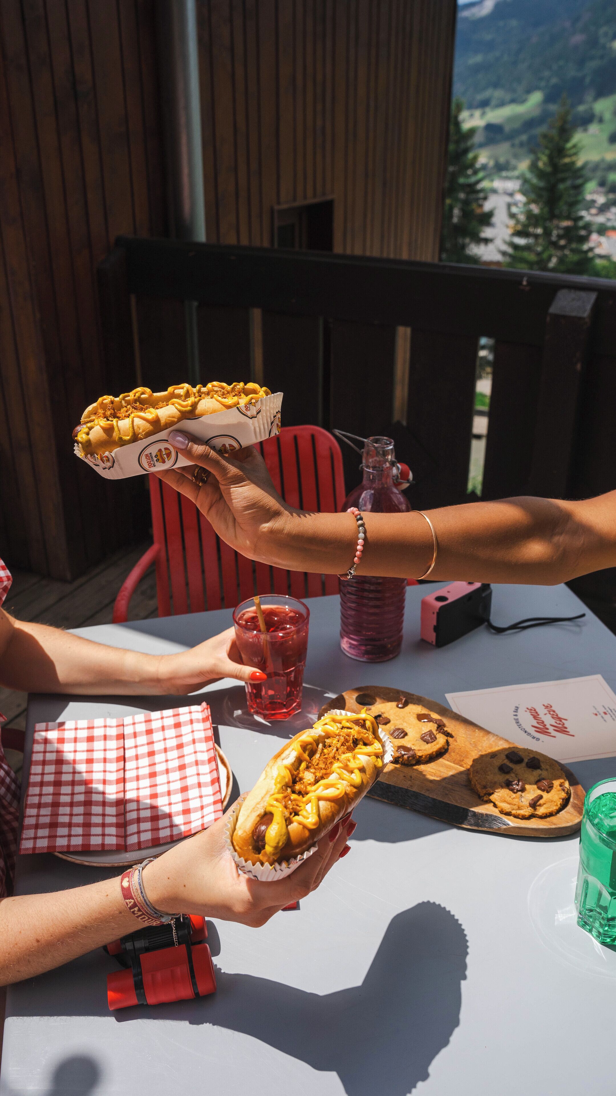 A table with a checkered tablecloth, a wooden cutting board with cookies, a glass of red drink, and a bottle of water.