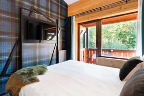 Un dormitorio con una cama grande, un televisor montado en la pared y una ventana con vistas a árboles.
