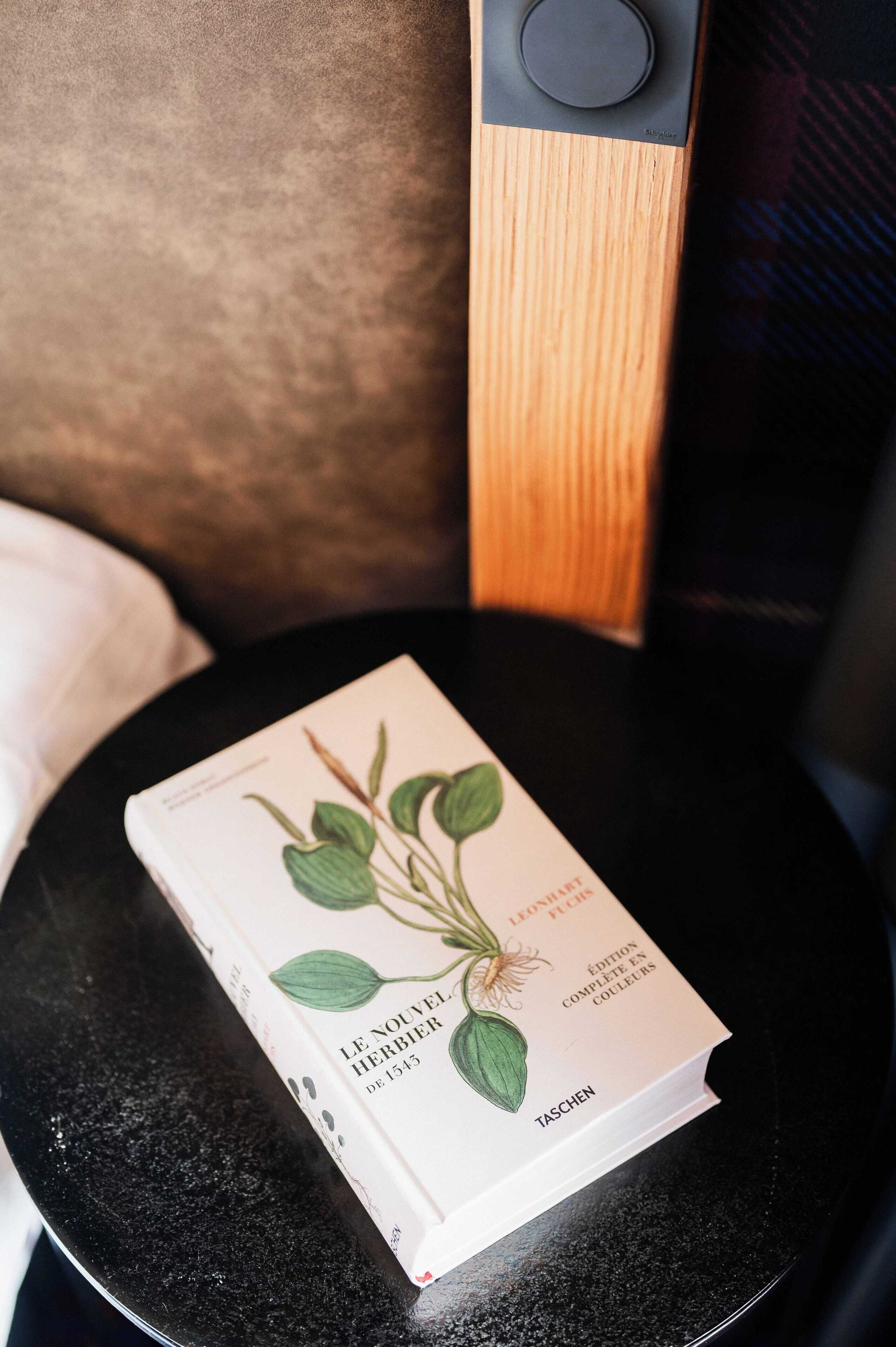 Un livre intitulé « Le Nouveau Herbier » est posé sur une table noire.