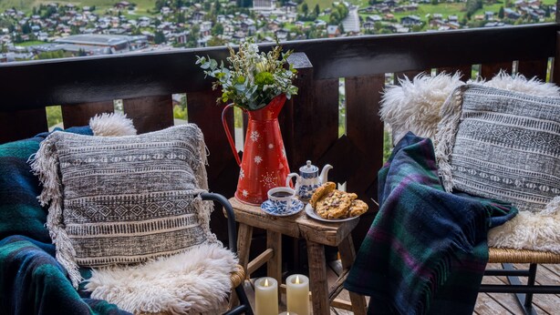 Una terraza de madera con dos sillas, una mesita con un florero, velas y un plato de galletas.