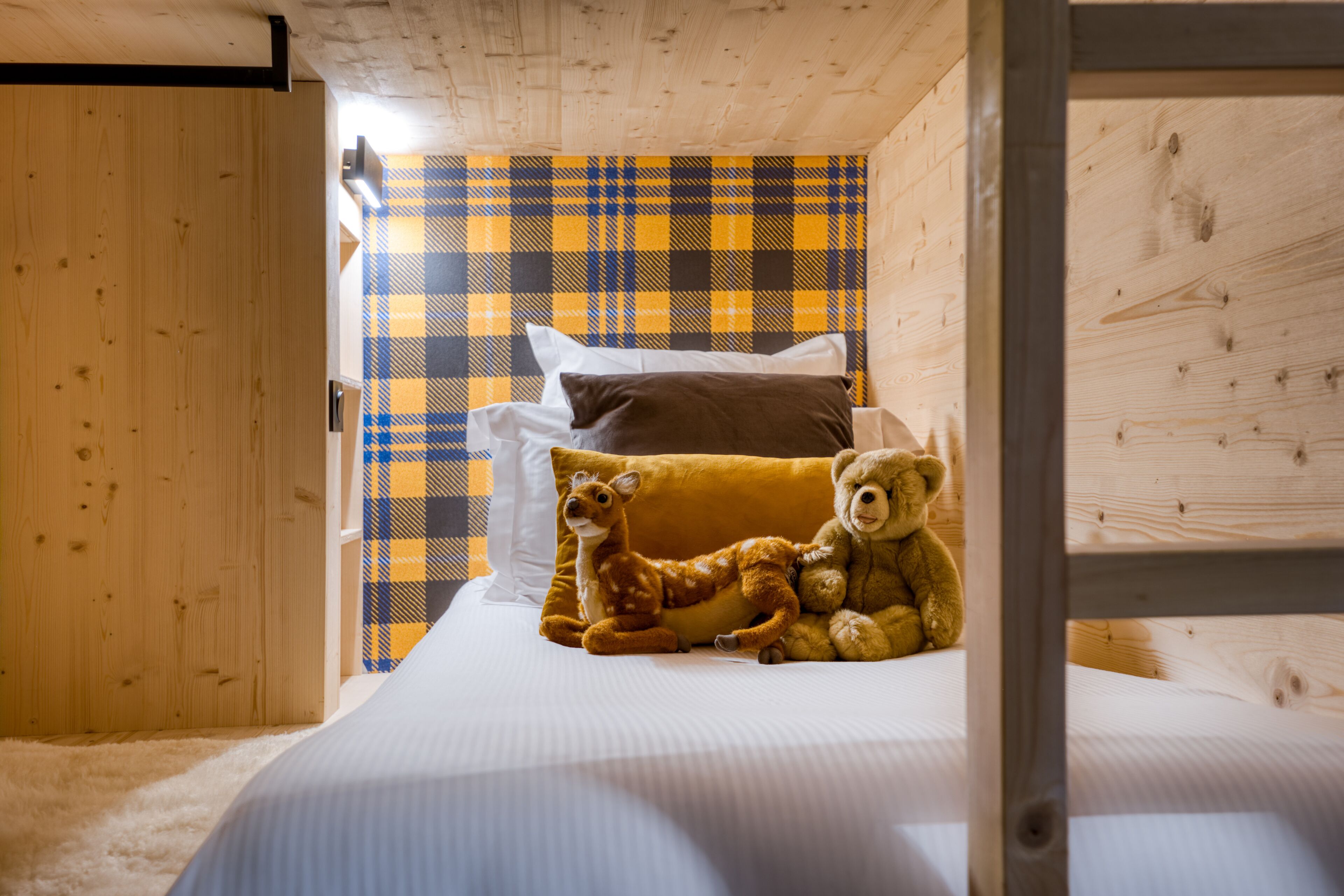 Une pièce en bois avec un lit, un mur à motifs écossais et un ours en peluche sur le lit.