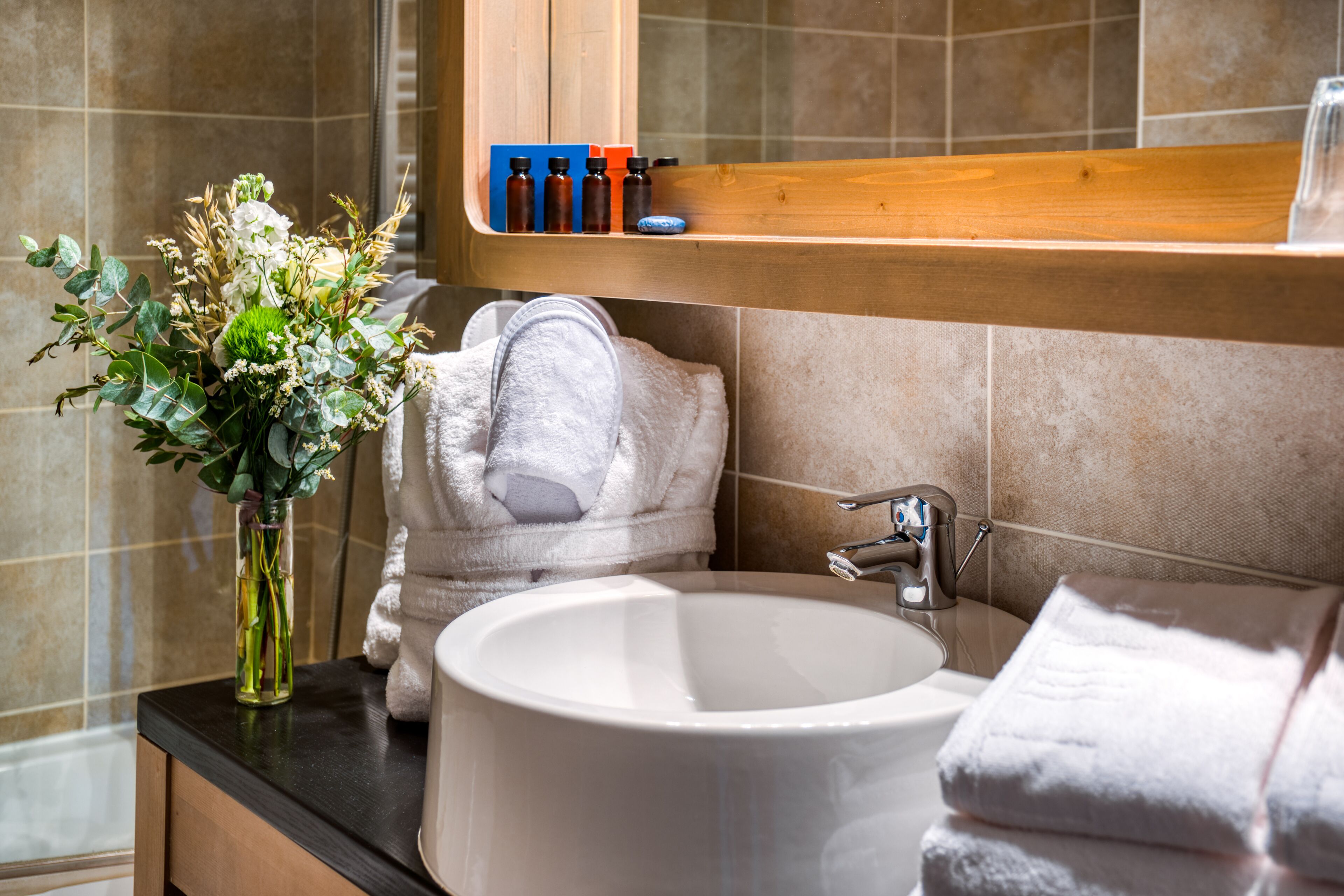 A bathroom with a white sink, a vase of flowers, and a towel rack with towels.