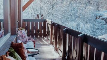 A wooden deck with a railing, covered in snow, overlooking a snowy landscape with trees.