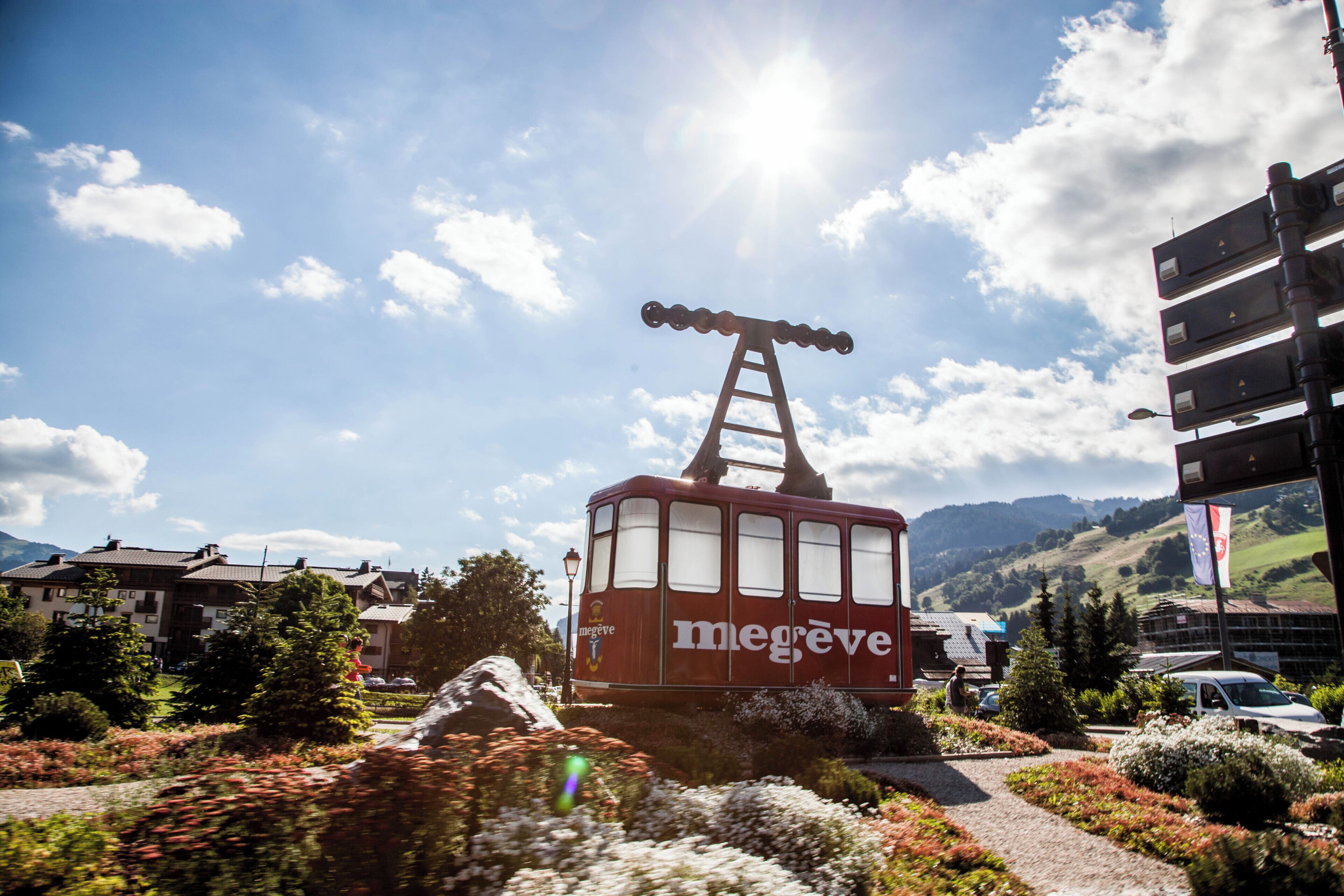 A red cable car with 'megève' branding, a ladder, and a clear sky with clouds.