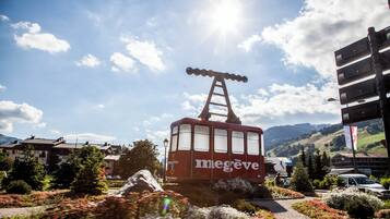A red cable car with 'megève' branding, a ladder, and a clear sky with clouds.