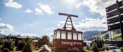 A red cable car with 'megève' branding, a ladder, and a clear sky with clouds.