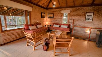 Una habitación acogedora con techo de madera, un conjunto de sofás, una chimenea y una ventana con vistas a un jardín.
