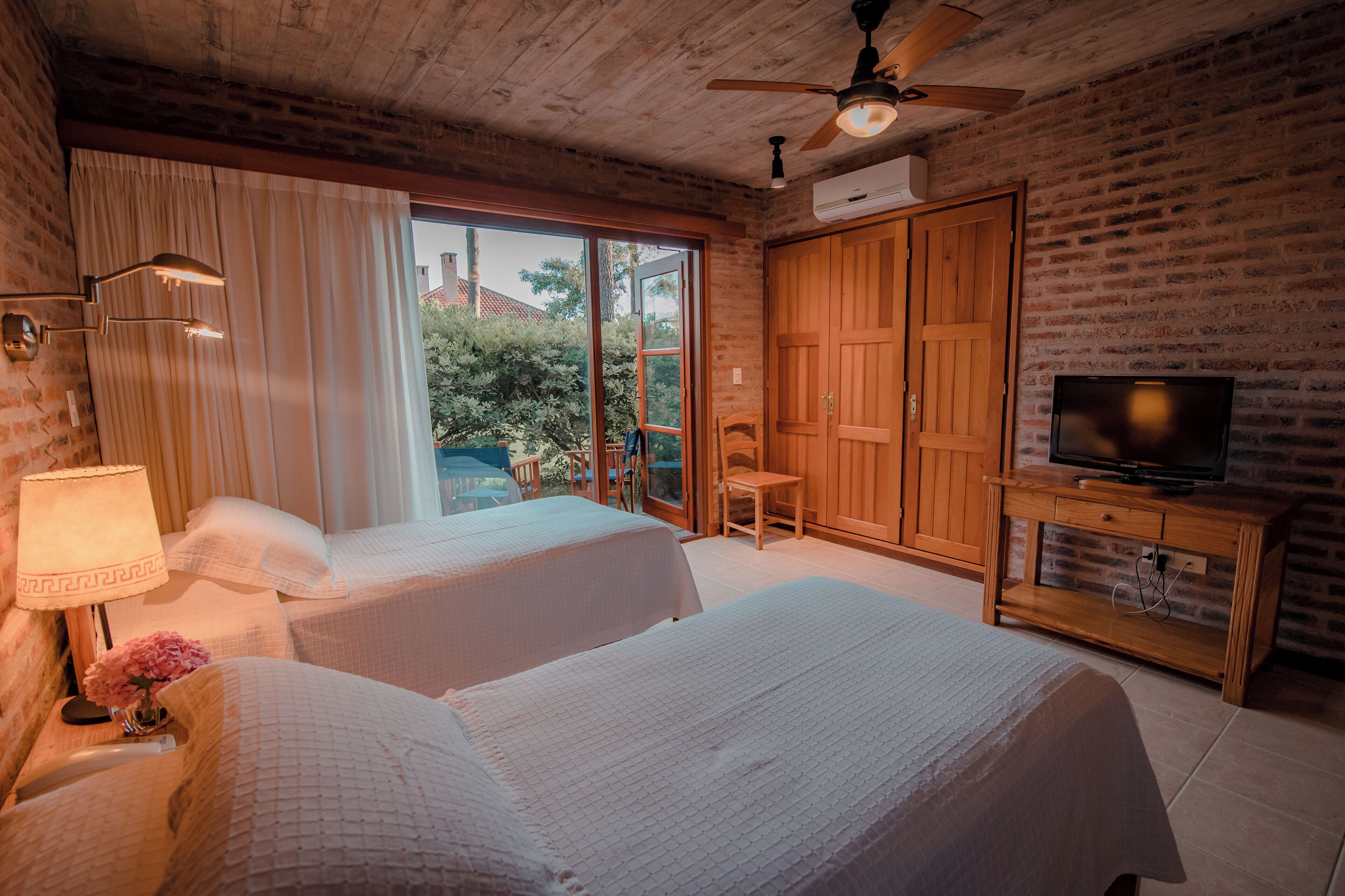 A hotel room with two beds, a TV, a wooden cabinet, and a ceiling fan.