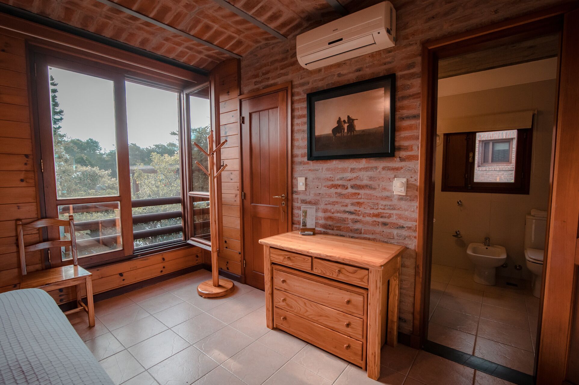 Um quarto de madeira com uma janela grande, um aparador de madeira, um cabideiro e um quadro pendurado na parede.