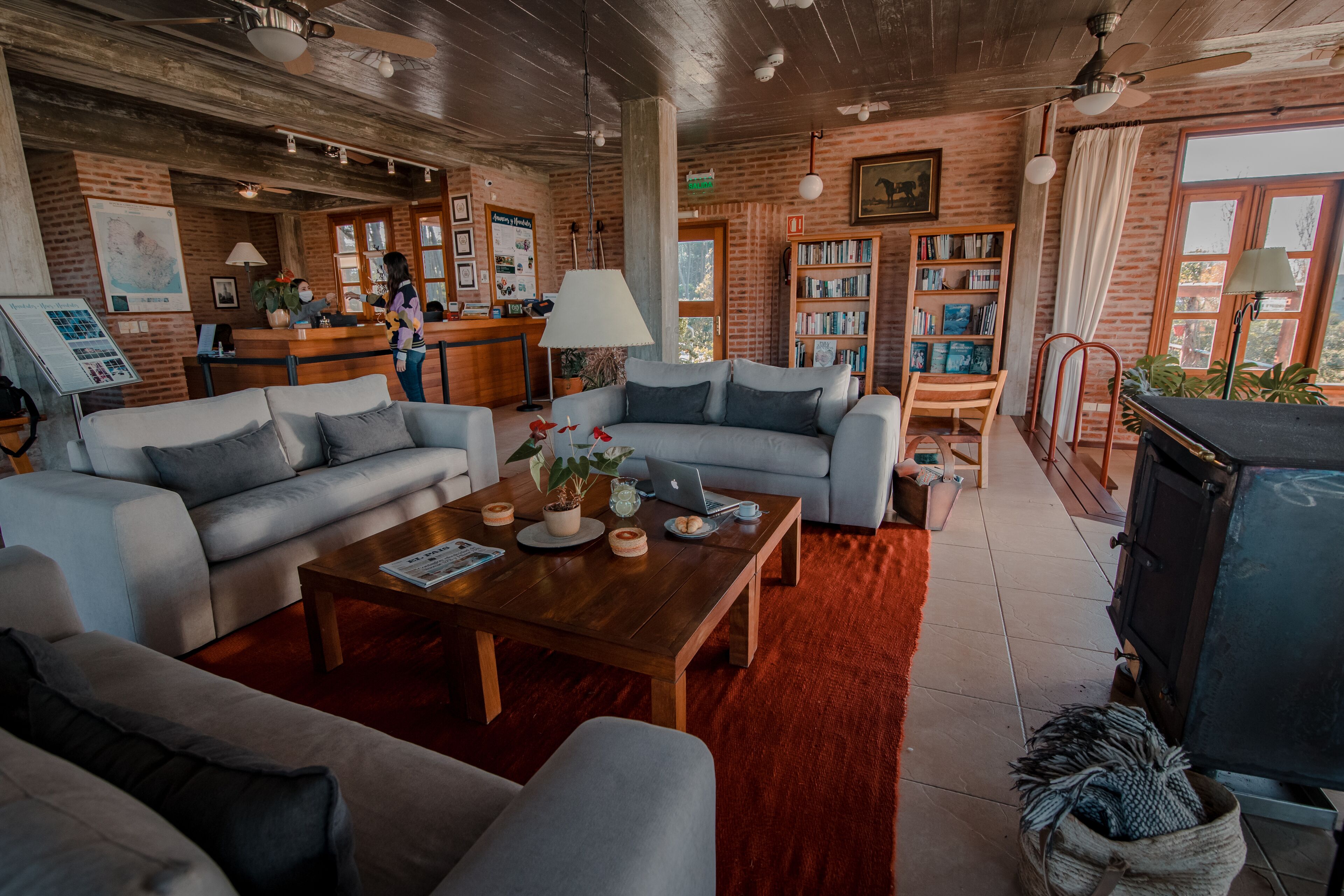A cozy living room with a wooden ceiling, a fireplace, a sofa set, a coffee table, and a bookshelf.