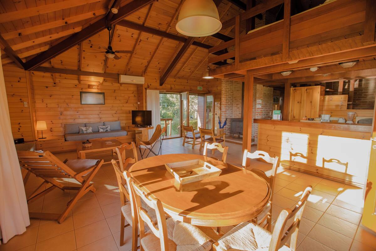 A wooden cabin interior with a dining area, kitchen, and seating space.