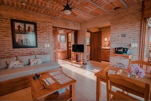 A cozy living room with a sofa, coffee table, and TV, connected to a kitchen area with wooden cabinets and a brick wall. - Il Belvedere Hotel (Punta del Este)