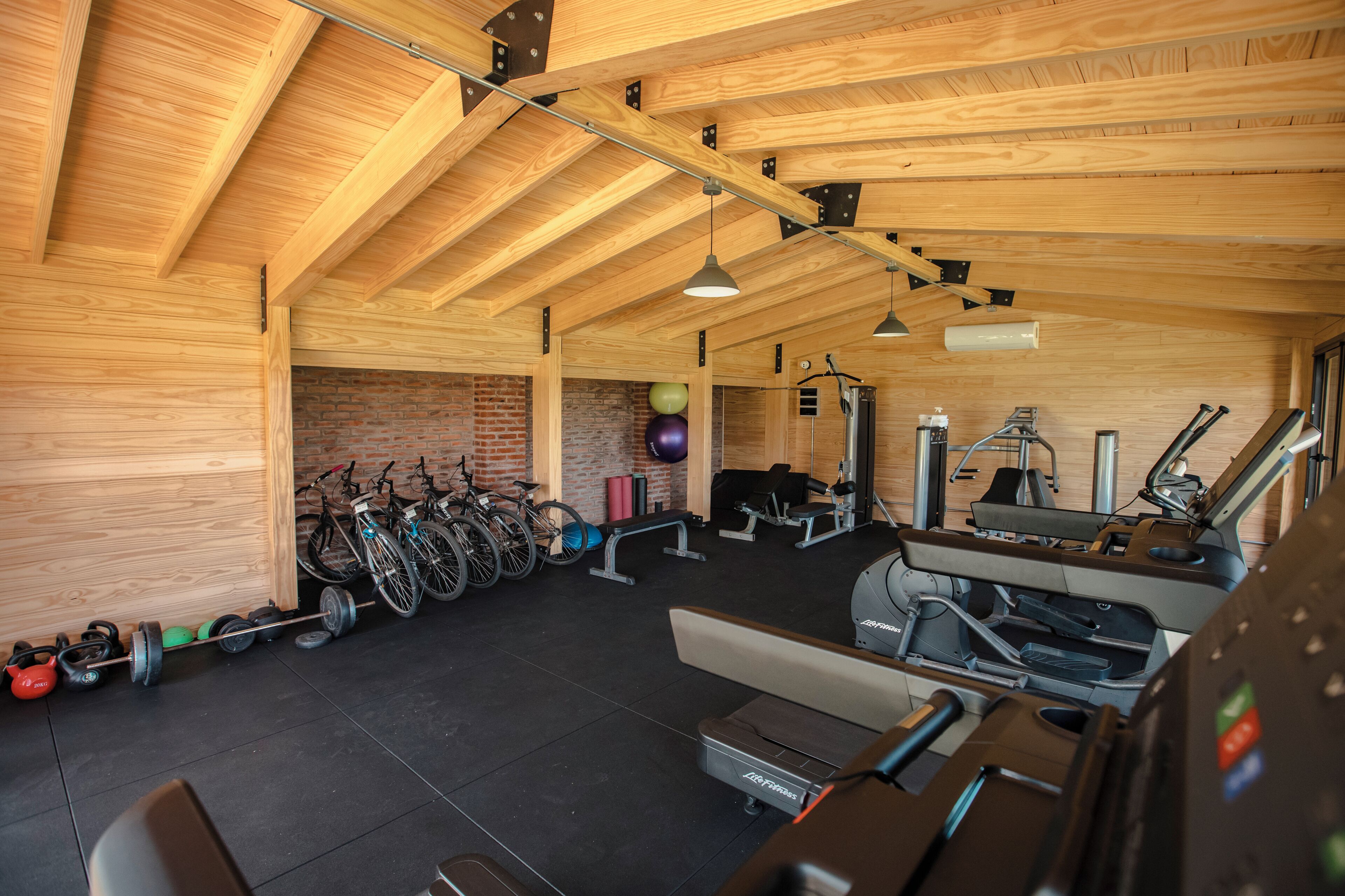 A gym with exercise equipment, a brick wall, and wooden beams.