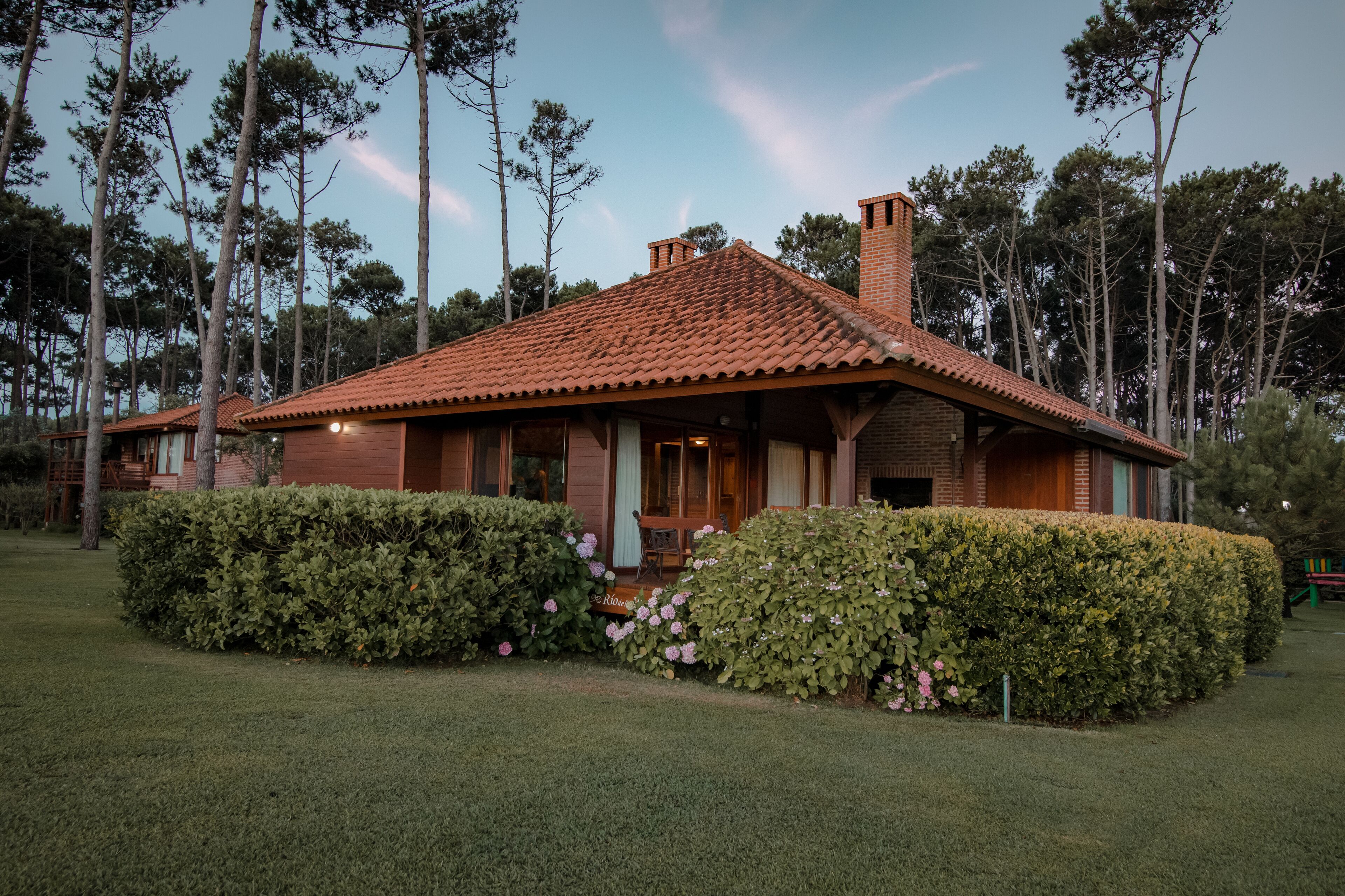 A single-story house with a red-tiled roof, surrounded by well-maintained hedges and a lawn.