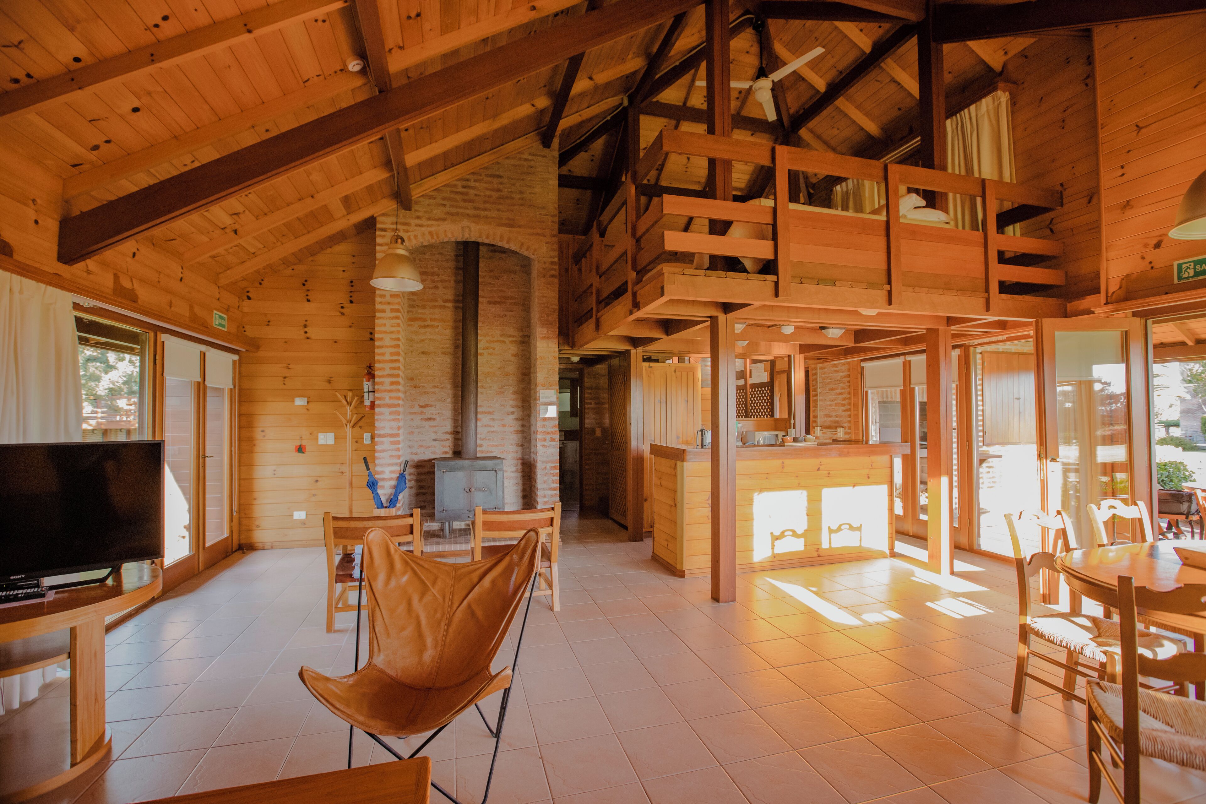 Interior de una cabaña de madera con televisor, asientos y chimenea.