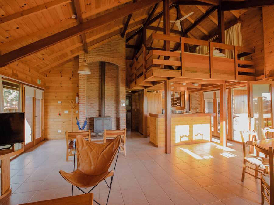 Interior de una cabaña de madera con televisor, asientos y chimenea.
