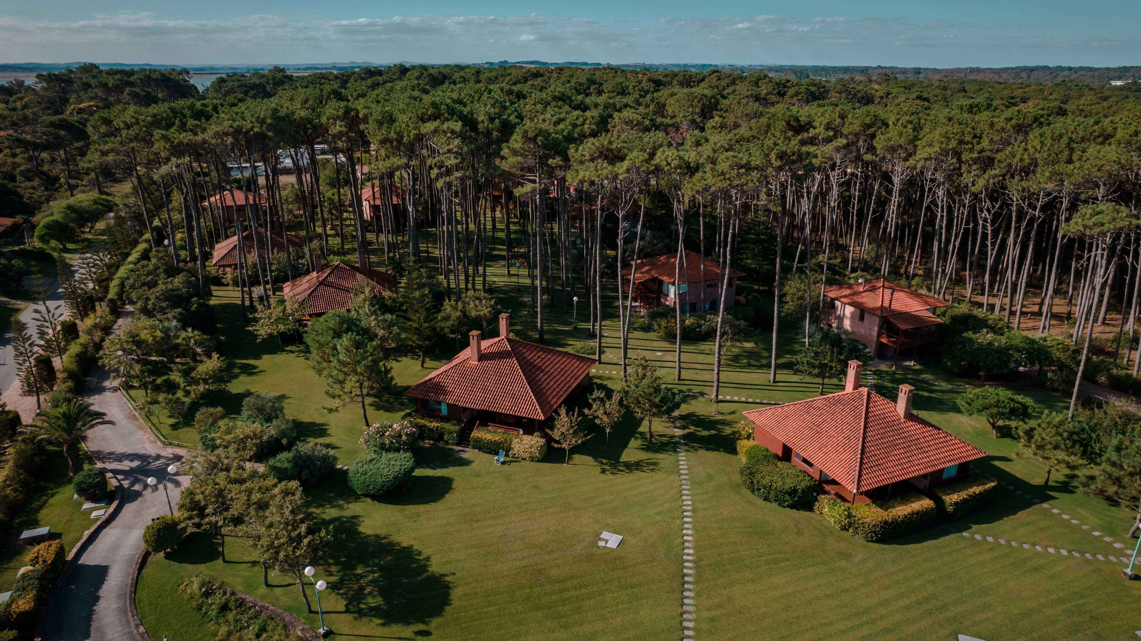 An aerial view of a residential area with multiple houses, each featuring a red-tiled roof, surrounded by dense greenery and a clear sky.