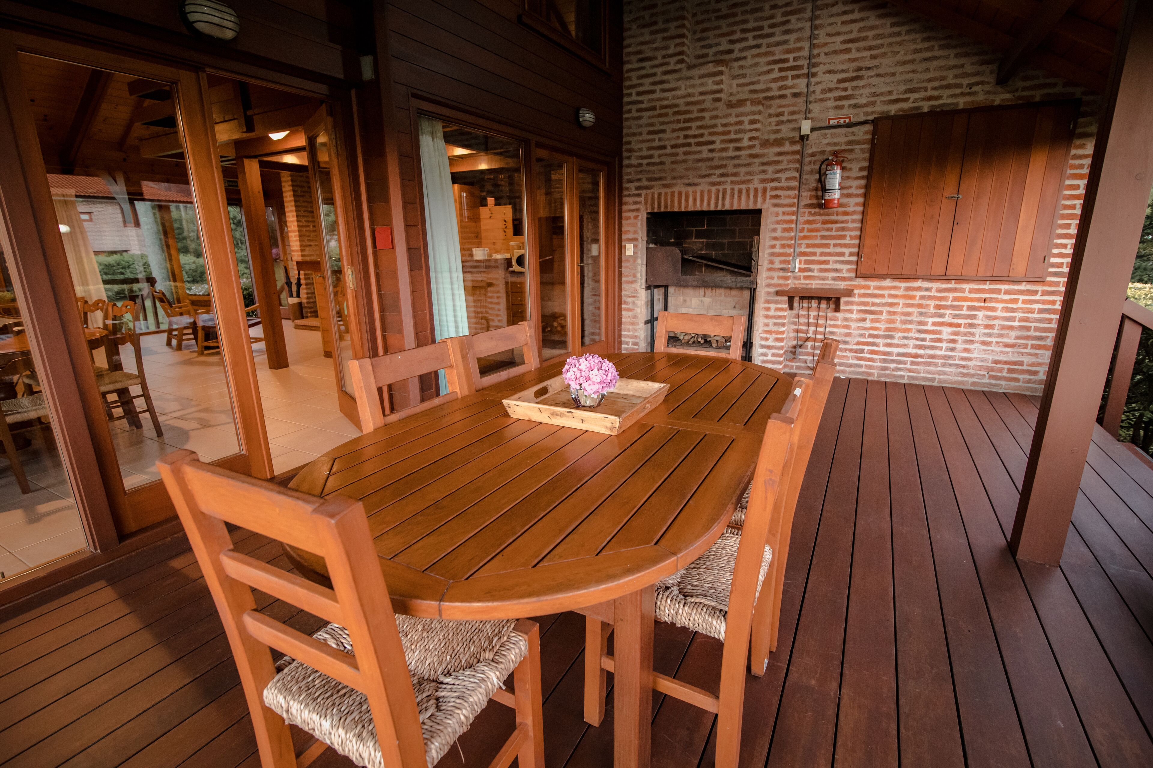 Una terraza de madera con una mesa redonda y sillas, una chimenea de ladrillo y un armario de madera.