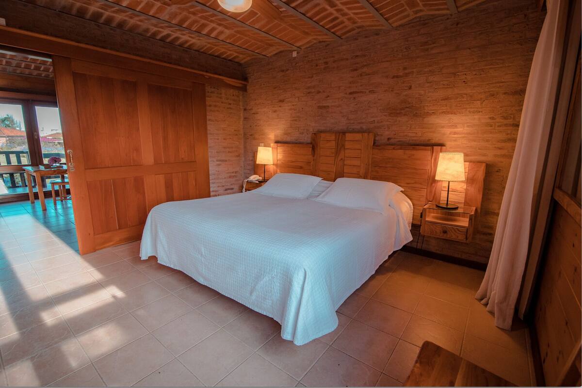 A large bed with a wooden headboard, two bedside lamps, and a view of a patio area with a table and chairs.